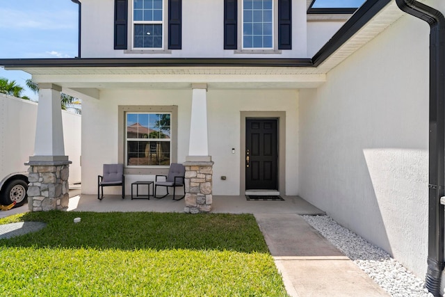 view of exterior entry with a porch and a lawn