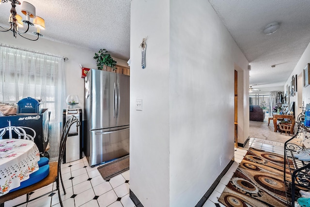 kitchen featuring stainless steel refrigerator, ceiling fan with notable chandelier, a textured ceiling, and light tile flooring