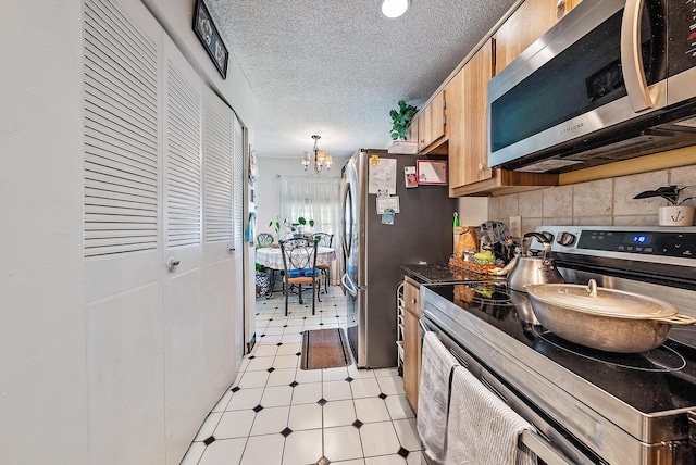 kitchen featuring an inviting chandelier, stainless steel appliances, light tile floors, tasteful backsplash, and a textured ceiling