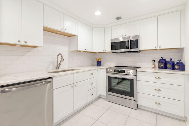 kitchen featuring sink, appliances with stainless steel finishes, decorative backsplash, light tile patterned floors, and white cabinets