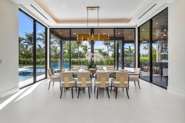 dining space with light tile patterned floors, a raised ceiling, a wall of windows, and plenty of natural light