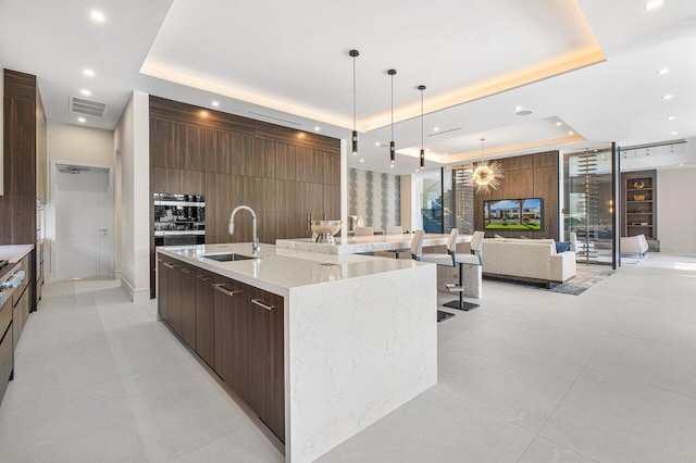 kitchen with hanging light fixtures, sink, a large island with sink, and a tray ceiling