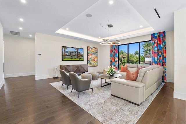 living room featuring dark hardwood / wood-style flooring, a raised ceiling, and a notable chandelier