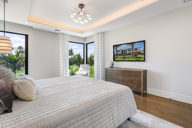 bedroom featuring hardwood / wood-style floors, a tray ceiling, and a notable chandelier