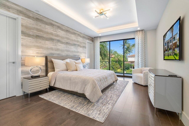 bedroom featuring access to outside, a tray ceiling, and dark wood-type flooring