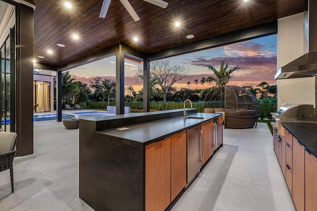 patio terrace at dusk with a grill, ceiling fan, exterior kitchen, and a wet bar