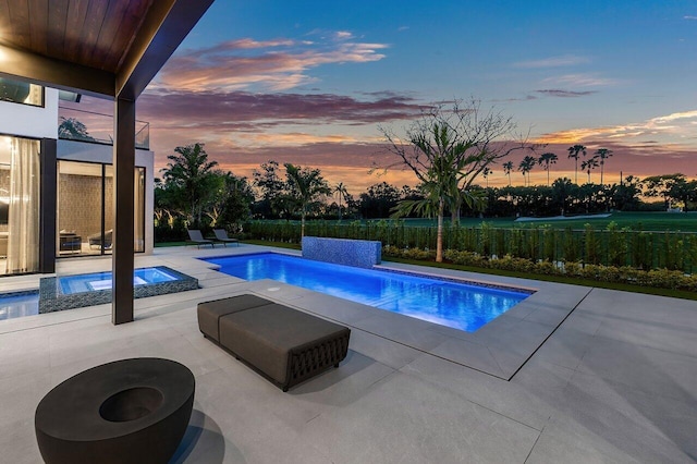 pool at dusk featuring a fire pit, a patio area, and an in ground hot tub