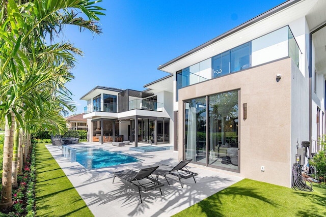 back of property featuring a balcony, a swimming pool with hot tub, and a patio