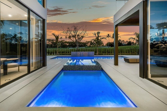 pool at dusk featuring an in ground hot tub and a patio area