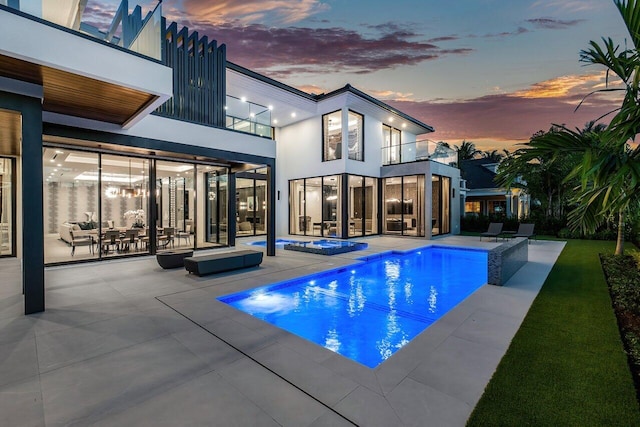 pool at dusk with a hot tub and a patio area