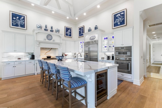 kitchen with wine cooler, white cabinets, light hardwood / wood-style flooring, stainless steel appliances, and light stone counters