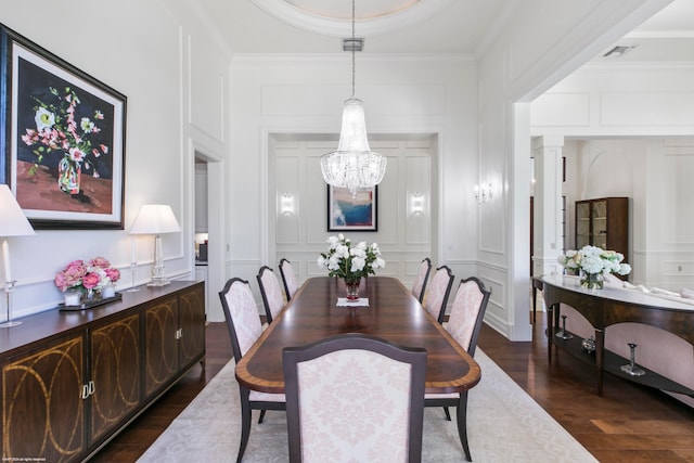 dining space with dark wood-type flooring, crown molding, a notable chandelier, and decorative columns