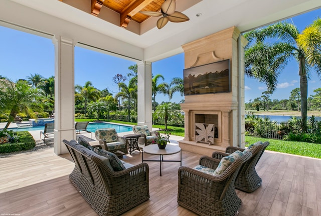 exterior space featuring a water view, a patio area, ceiling fan, and an outdoor living space with a fireplace