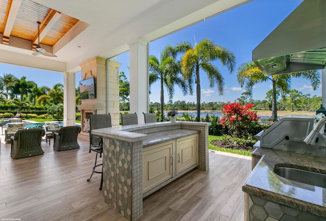 exterior space featuring a bar, a water view, an outdoor kitchen, area for grilling, and ceiling fan