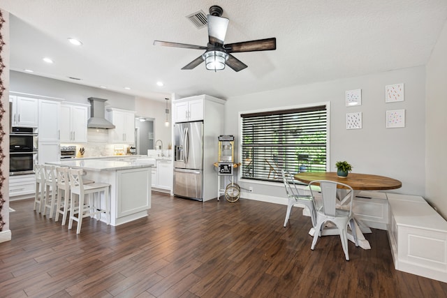 kitchen featuring dark hardwood / wood-style flooring, appliances with stainless steel finishes, a center island, and wall chimney exhaust hood