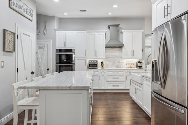 kitchen featuring light stone counters, white cabinets, dark hardwood / wood-style flooring, stainless steel appliances, and premium range hood