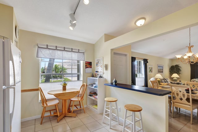 kitchen featuring white refrigerator, a chandelier, kitchen peninsula, light tile floors, and track lighting