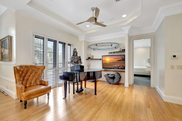 sitting room with a raised ceiling, ceiling fan, crown molding, and light wood-type flooring