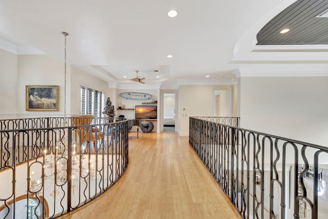 corridor with a tray ceiling, light wood-type flooring, and ornamental molding