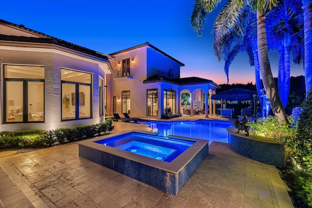 pool at dusk with an in ground hot tub and a patio area