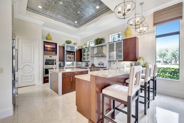 kitchen with a center island with sink, crown molding, wall chimney exhaust hood, and a tray ceiling