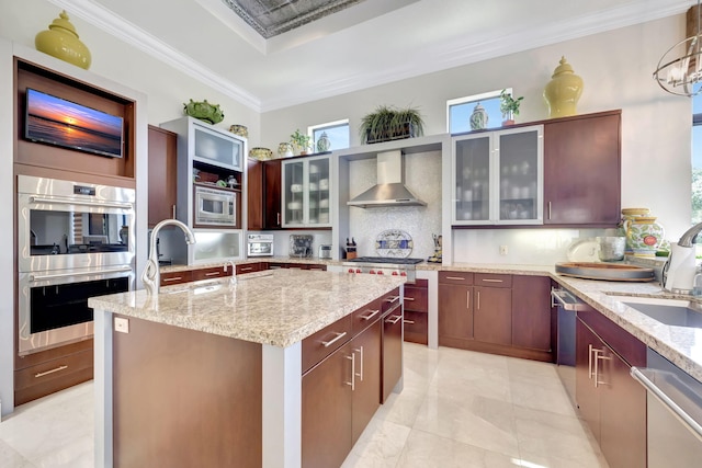 kitchen featuring wall chimney exhaust hood, backsplash, stainless steel appliances, light tile floors, and a center island with sink