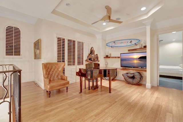 sitting room featuring ceiling fan, a tray ceiling, light wood-type flooring, and decorative columns