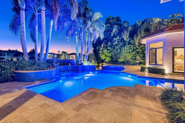 pool at dusk with a patio and a hot tub