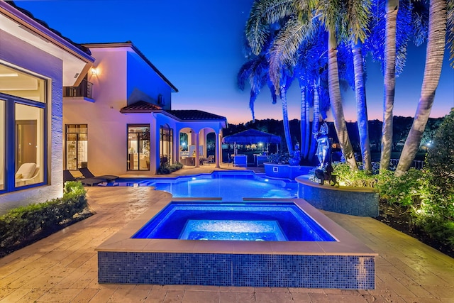 pool at dusk featuring an in ground hot tub and a patio