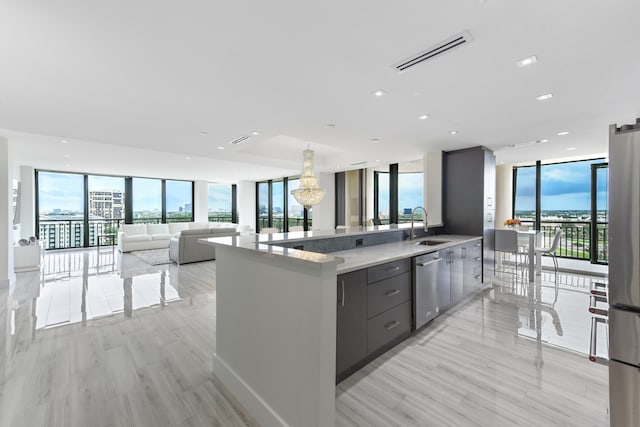 kitchen with gray cabinetry, appliances with stainless steel finishes, an island with sink, a wall of windows, and sink