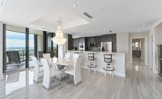 dining area with a tray ceiling, a chandelier, light hardwood / wood-style floors, and a wall of windows