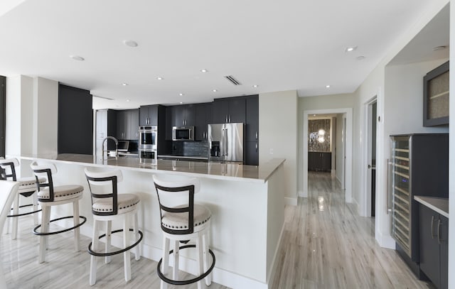 kitchen featuring stainless steel appliances, light wood-type flooring, a kitchen bar, and backsplash