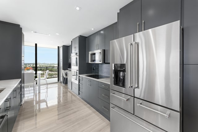 kitchen featuring stainless steel appliances, expansive windows, tasteful backsplash, light stone countertops, and light wood-type flooring