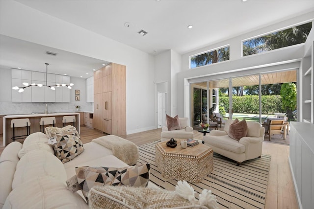 living room with sink, light hardwood / wood-style floors, a chandelier, and a towering ceiling