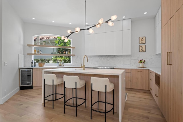 kitchen with backsplash, light hardwood / wood-style flooring, a center island with sink, and beverage cooler