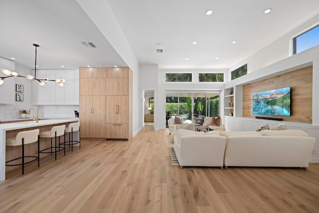 living room featuring a healthy amount of sunlight, light wood-type flooring, a chandelier, and a towering ceiling