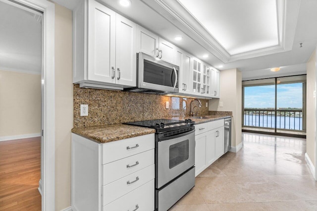 kitchen featuring appliances with stainless steel finishes, white cabinetry, dark stone countertops, decorative backsplash, and crown molding