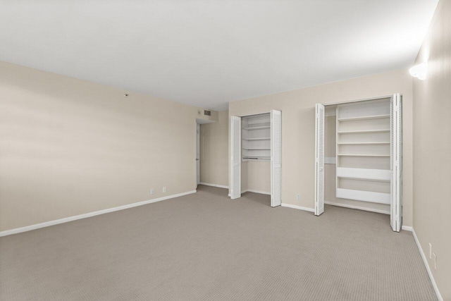 unfurnished bedroom featuring light carpet and two closets