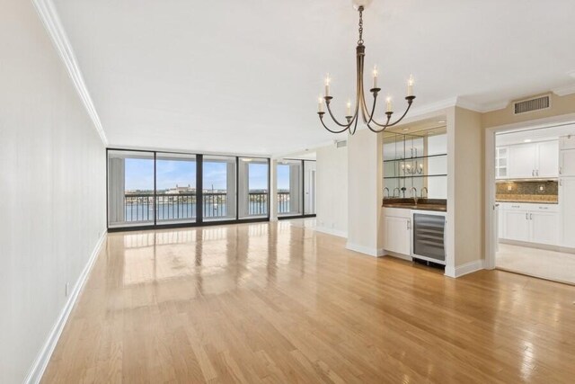 dining space featuring crown molding, a water view, light wood-type flooring, and a notable chandelier