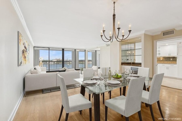 dining area with a water view, ornamental molding, a chandelier, and light hardwood / wood-style flooring