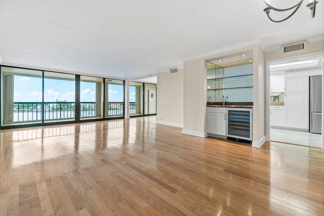 unfurnished living room featuring wine cooler, ornamental molding, expansive windows, and light hardwood / wood-style floors