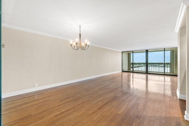 spare room with a notable chandelier, a wall of windows, ornamental molding, and wood-type flooring