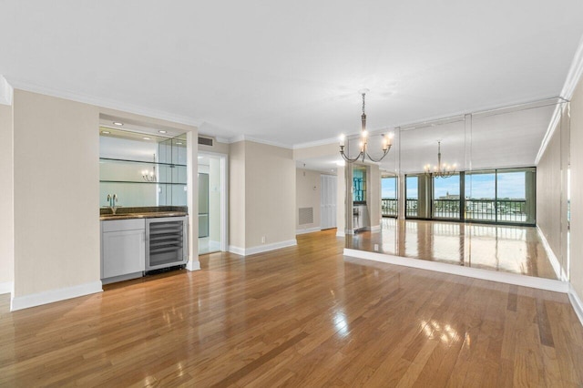 unfurnished living room with ornamental molding, beverage cooler, a chandelier, and indoor wet bar