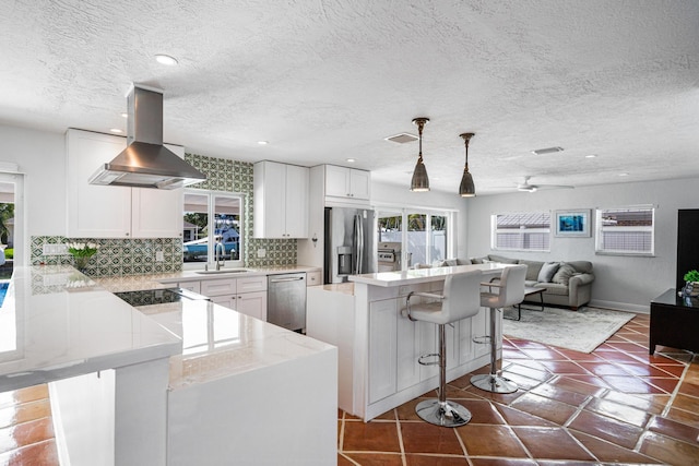 kitchen featuring white cabinetry, island exhaust hood, appliances with stainless steel finishes, and a breakfast bar area