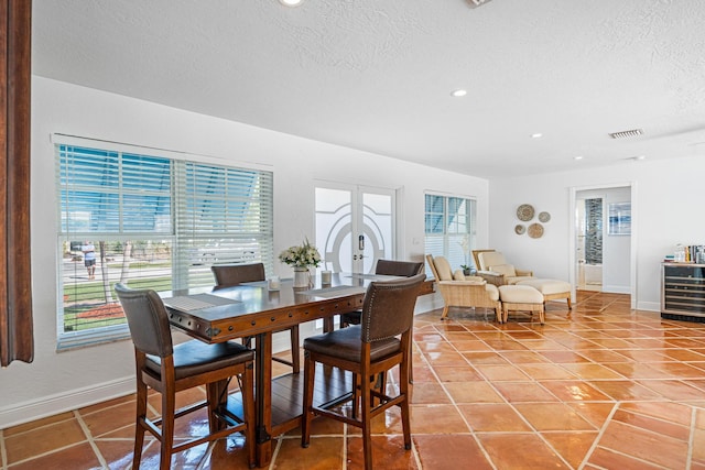 tiled dining space featuring beverage cooler, a textured ceiling, and french doors