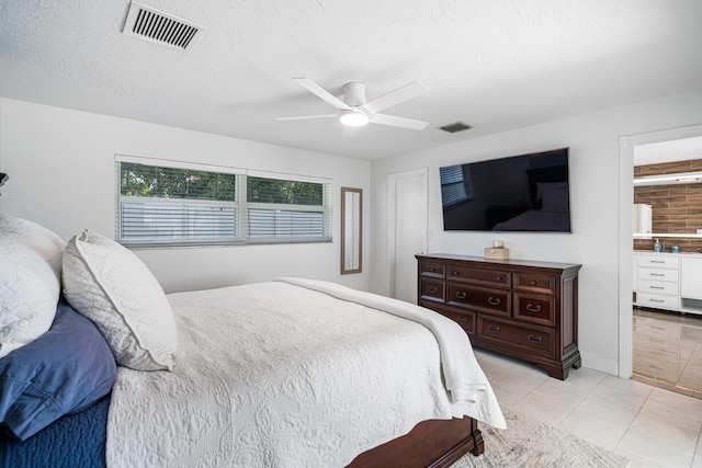 tiled bedroom featuring a textured ceiling, ceiling fan, and ensuite bath