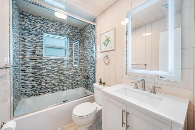 full bathroom with tile walls, bath / shower combo with glass door, vanity, decorative backsplash, and toilet