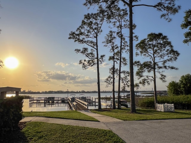 view of property's community featuring a water view, a dock, and a lawn