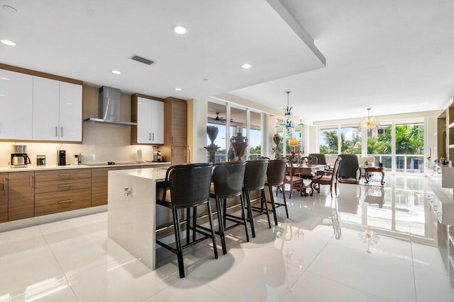 kitchen with decorative light fixtures, white cabinetry, light tile floors, and wall chimney exhaust hood