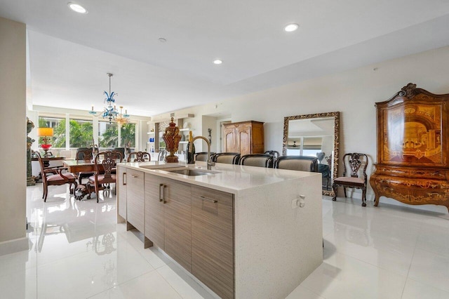 kitchen featuring a notable chandelier, light stone counters, light tile floors, and a kitchen island with sink